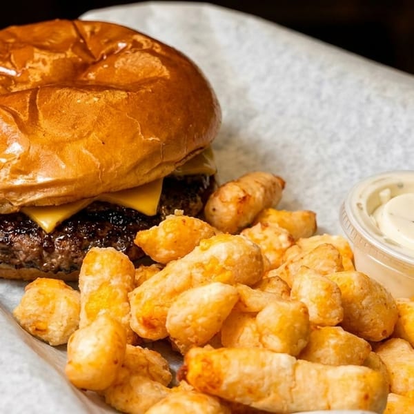 Cheeseburger with tater tots and two dipping sauces served in a basket lined with white paper.