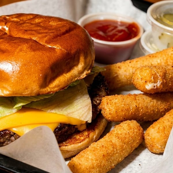 Cheeseburger with lettuce, mozzarella sticks, ketchup, and tartar sauce in a black tray.
