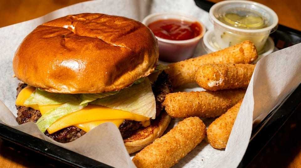 Cheeseburger with lettuce, mozzarella sticks, ketchup, and tartar sauce in a black tray.