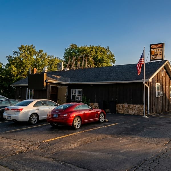 Exterior of Shoots Bar & Grill with a parking lot full of cars and a large white tent.